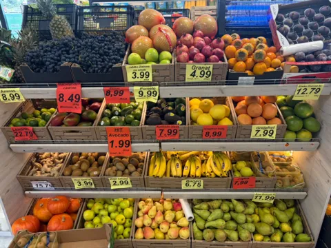 Regał z owocami: winogrona, granaty, awokado, banany i kiwi